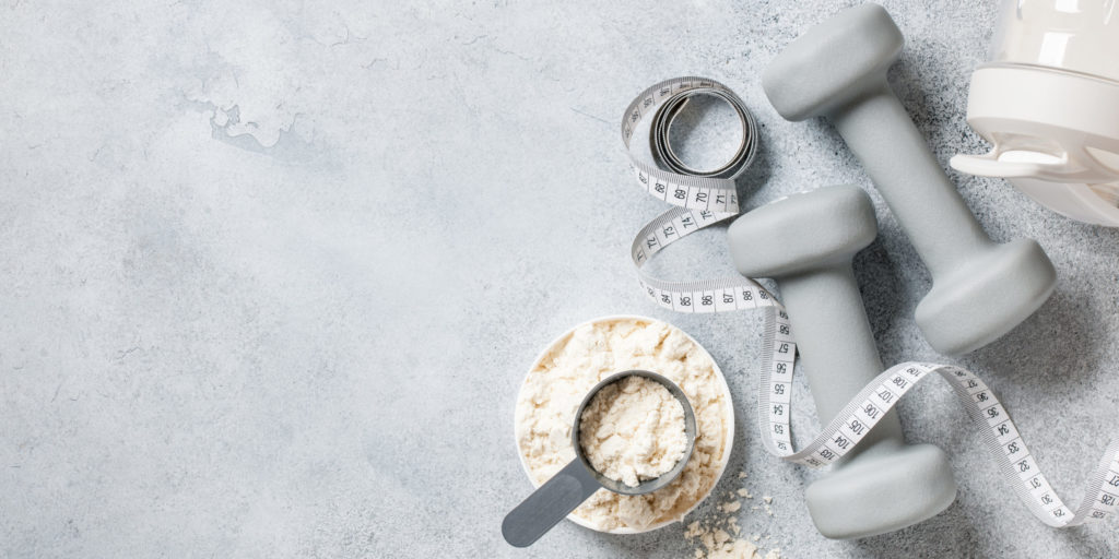Whey protein powder, shaker with protein cocktail and dumbbells