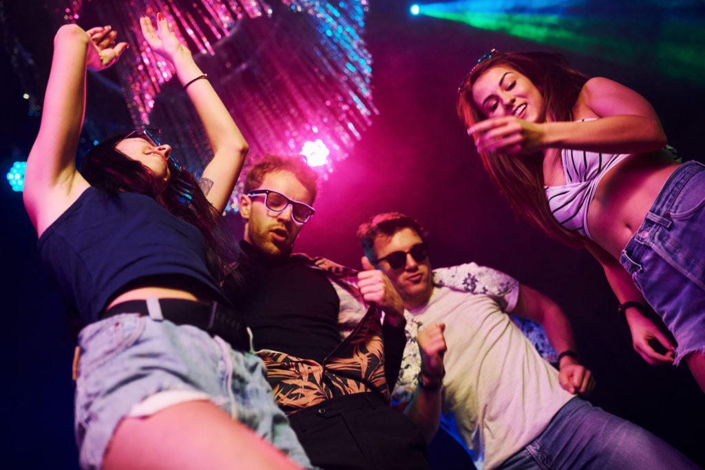 View from below of young people that having fun in night club with colorful laser lights